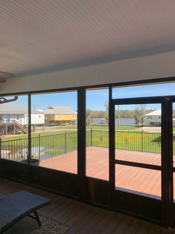 Covered patio overlooking a green backyard and neighboring houses, with a wooden deck and glass doors