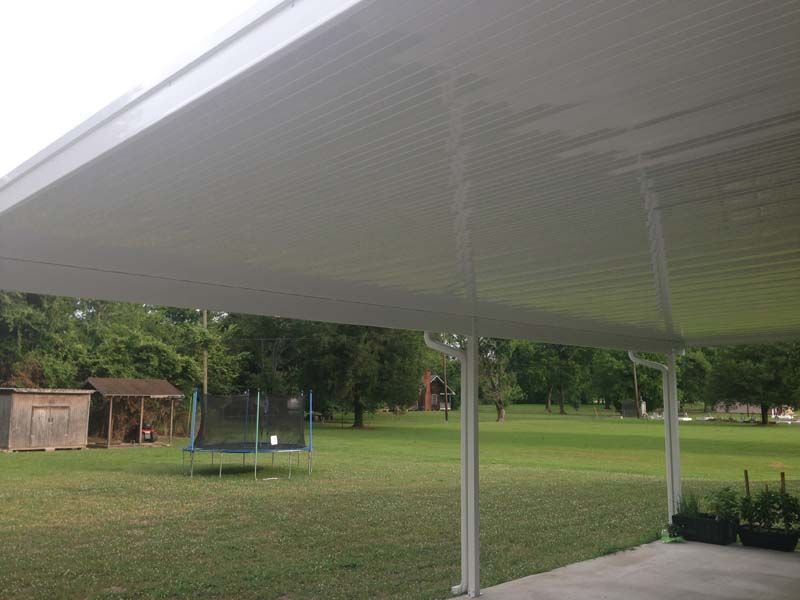 Shaded park under a large white canopy with a trampoline and small shed on a grassy lawn.