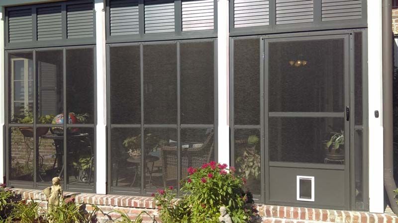 Patio with large screened windows, white wall, and potted plants along a brick ledge