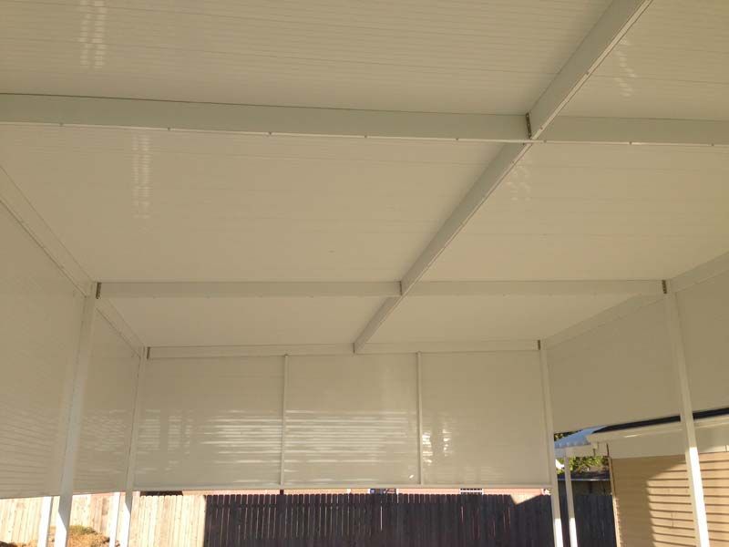 White covered patio ceiling with metal beams and shade blinds, plus a glimpse of a house wall.