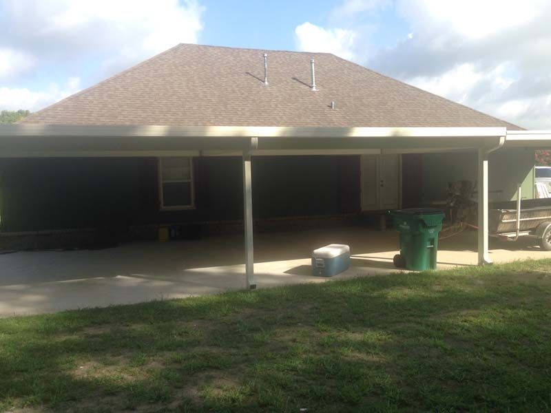 Backyard patio with covered porch, lawn, trash bins, and a small step stool