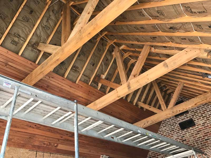 Wooden roof trusses and beams inside an unfinished attic with exposed insulation and brick wall