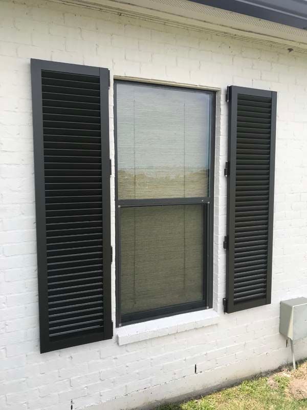 White brick house exterior with a window and black shutters on either side
