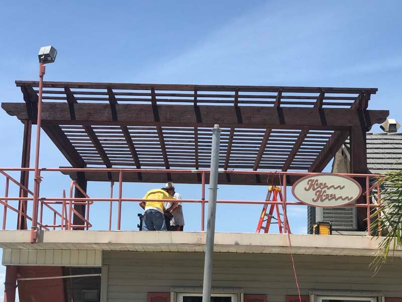 Workers on a rooftop installing a metal pergola frame above a building entrance.