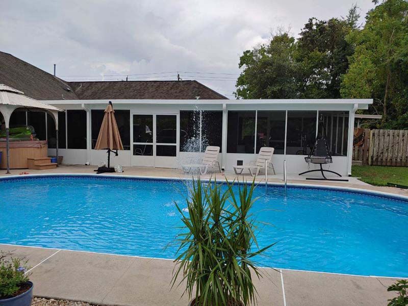 Backyard pool with patio furniture and white-covered house under cloudy sky