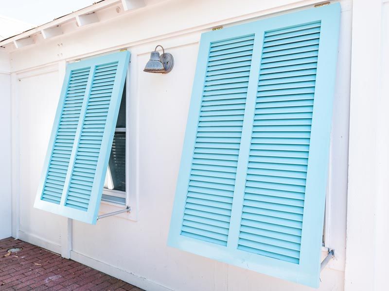 Light blue shutters on a white house, with one open over a window.