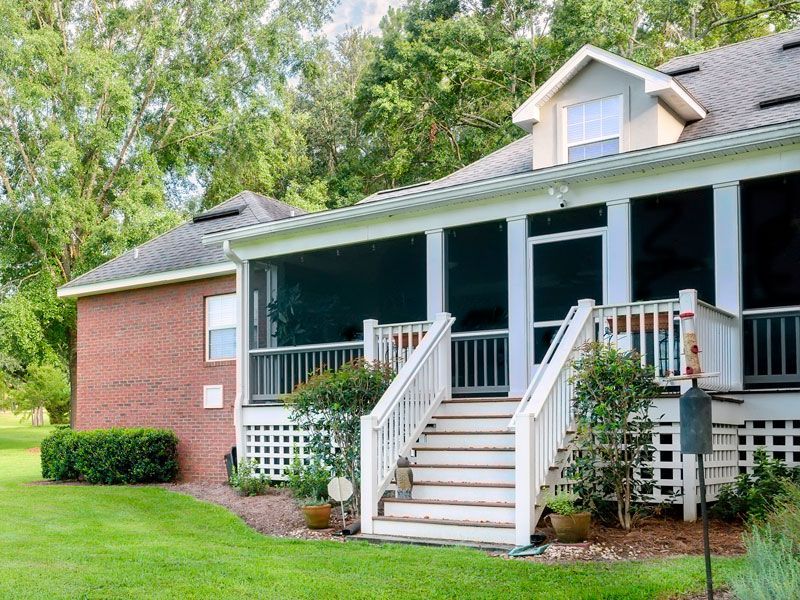 Brick house with a covered porch, white stairs, and green lawn surrounded by trees.
