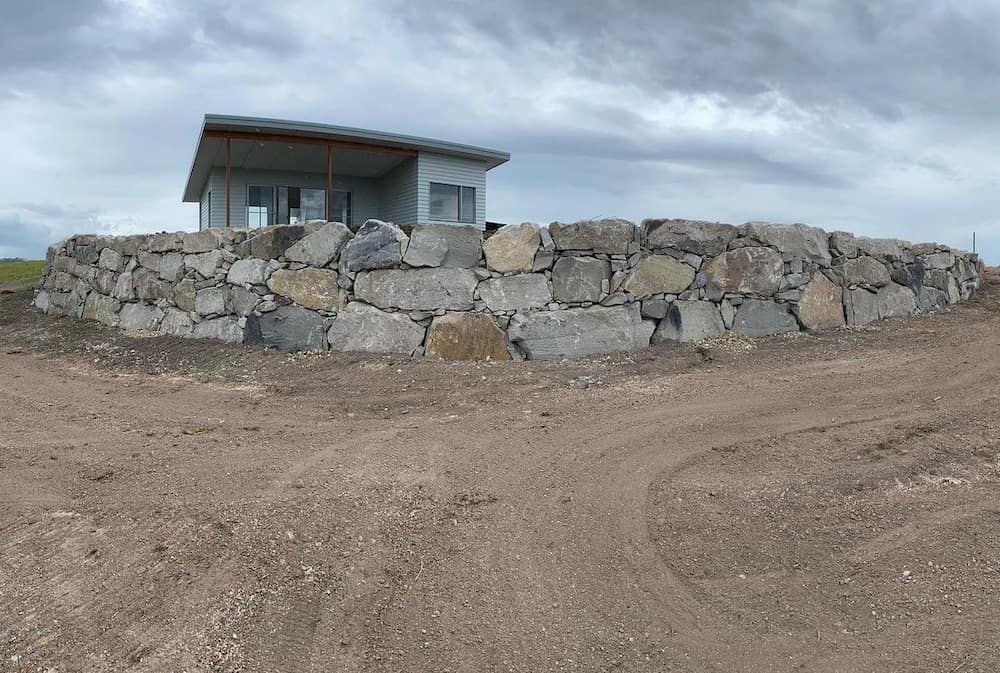 A Stone Wall With A House In The Background — J & M Bashforth & Sons In Brunswick Heads, NSW