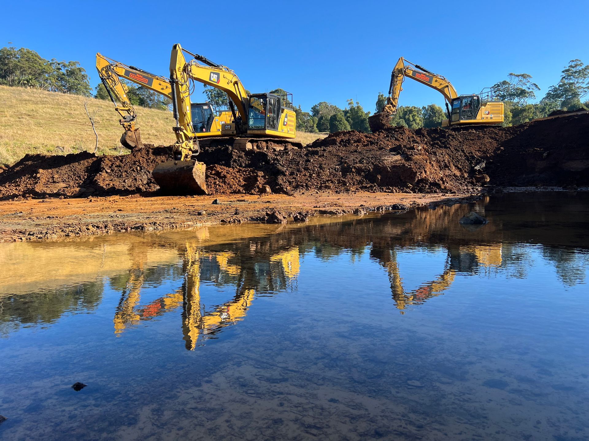 Two Excavators In Front And Reflecting From A Pond— J & M Bashforth & Sons In Brunswick Heads, NSW