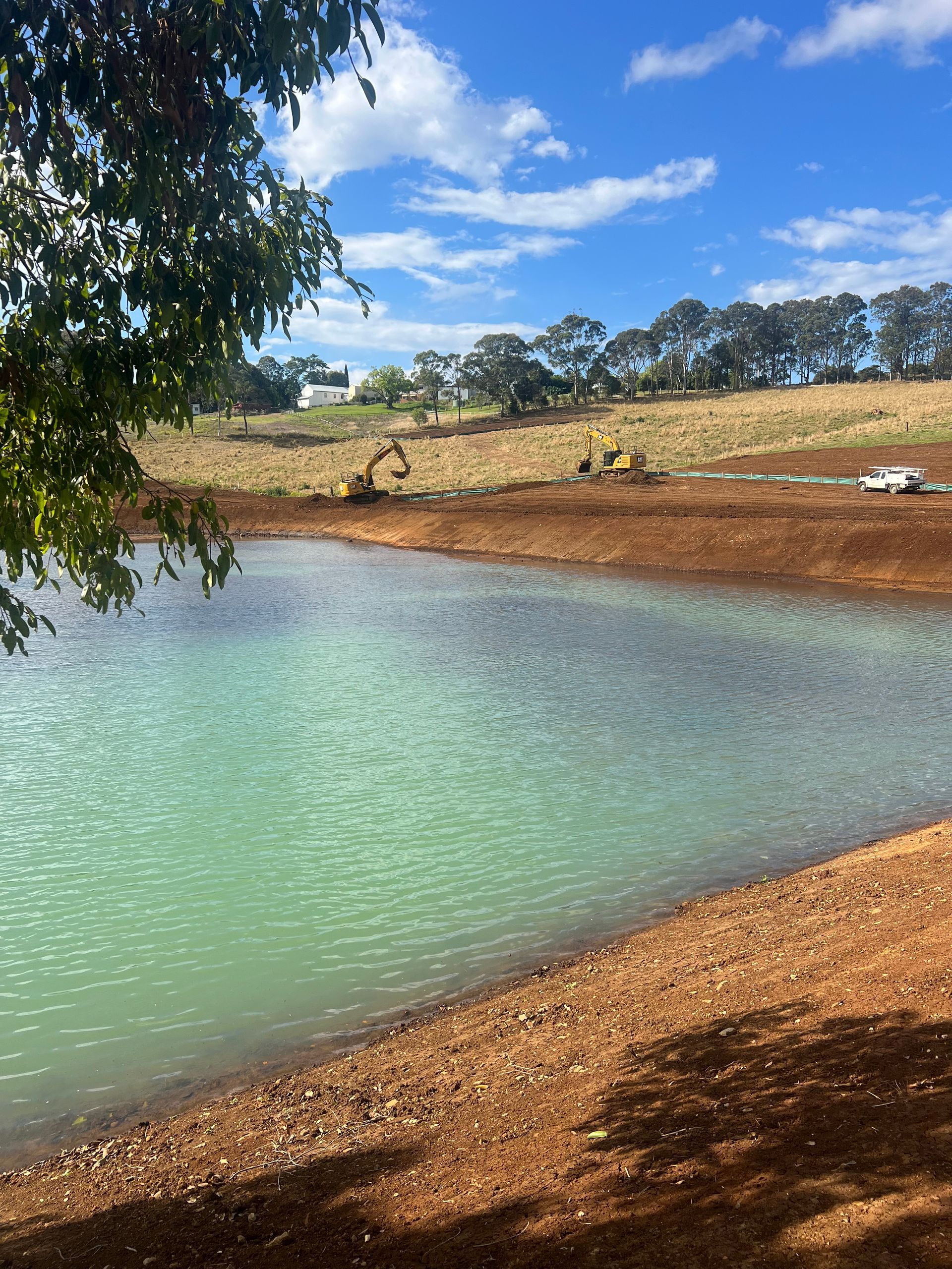 A large body of water surrounded by dirt and trees on a sunny day.