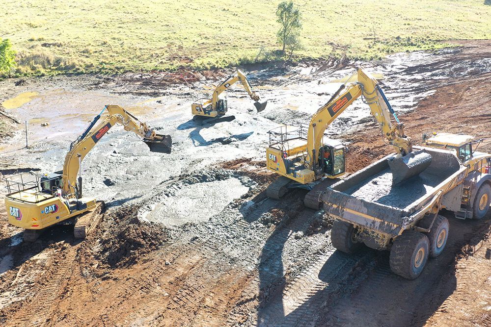 Three Yellow Excavators Load a Large Dump Truck in a Construction Site — J & M Bashforth & Sons In Byron Bay, NSW