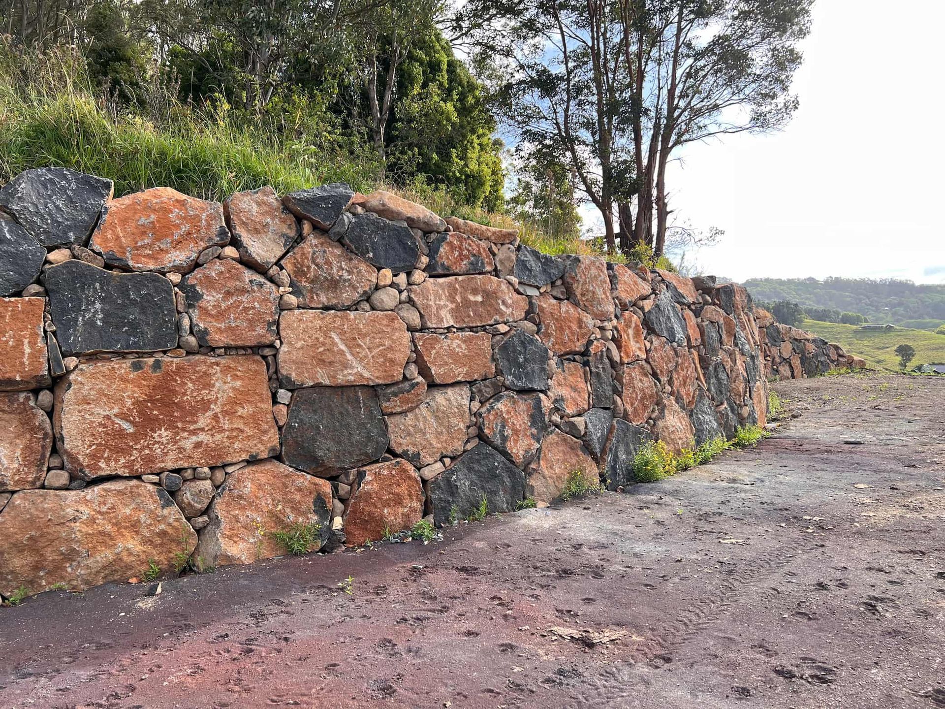 A Stone Wall Along a Dirt Road with Trees — J & M Bashforth & Sons In Yamba, NSW