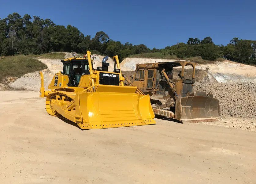A Yellow Bulldozer Is Parked Next to Another Bulldozer in A Dirt Field  — J & M Bashforth & Sons In Brunswick Heads, NSW