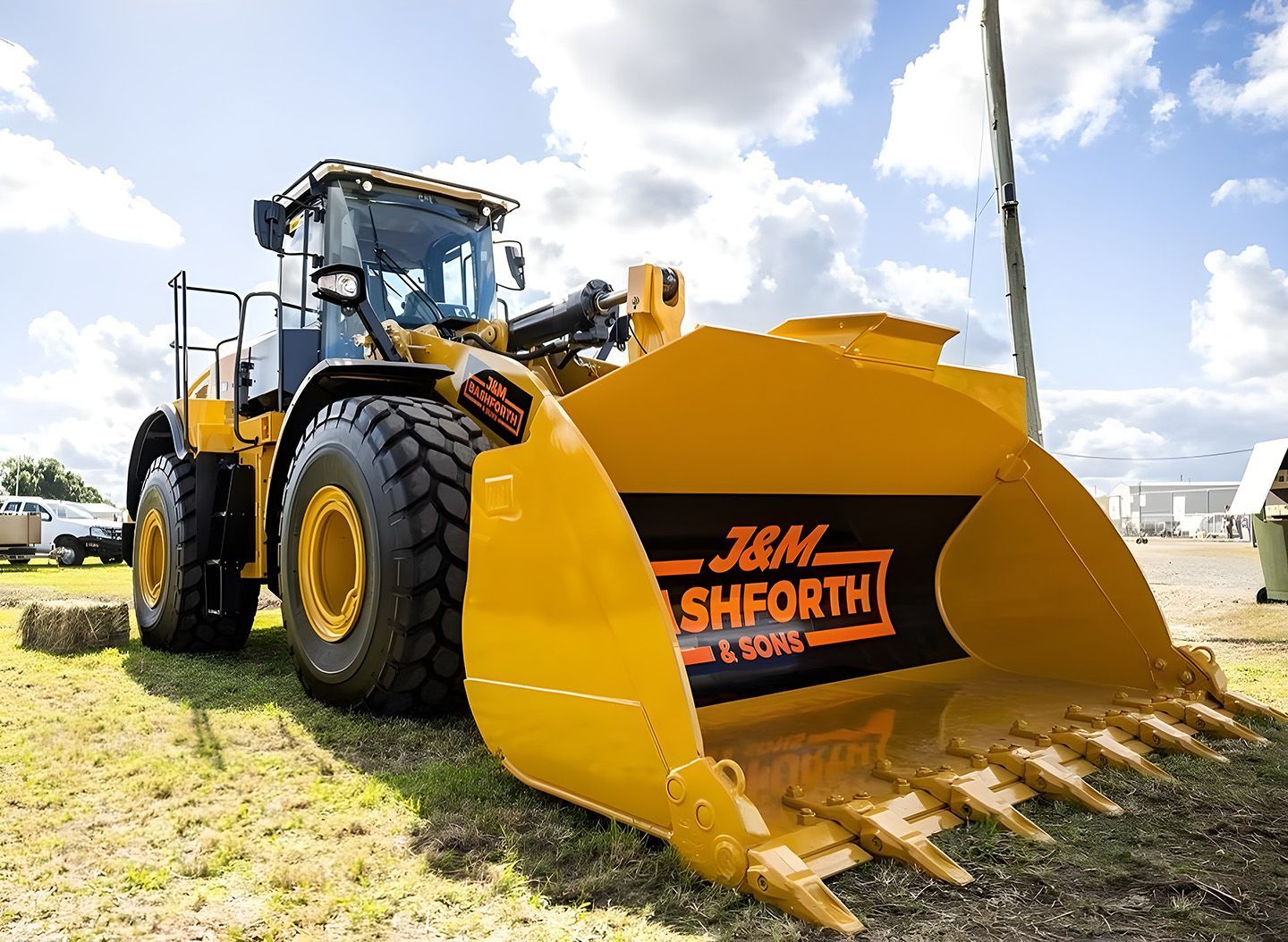 Yellow wheel loader with large bucket parked on grass under a cloudy sky
