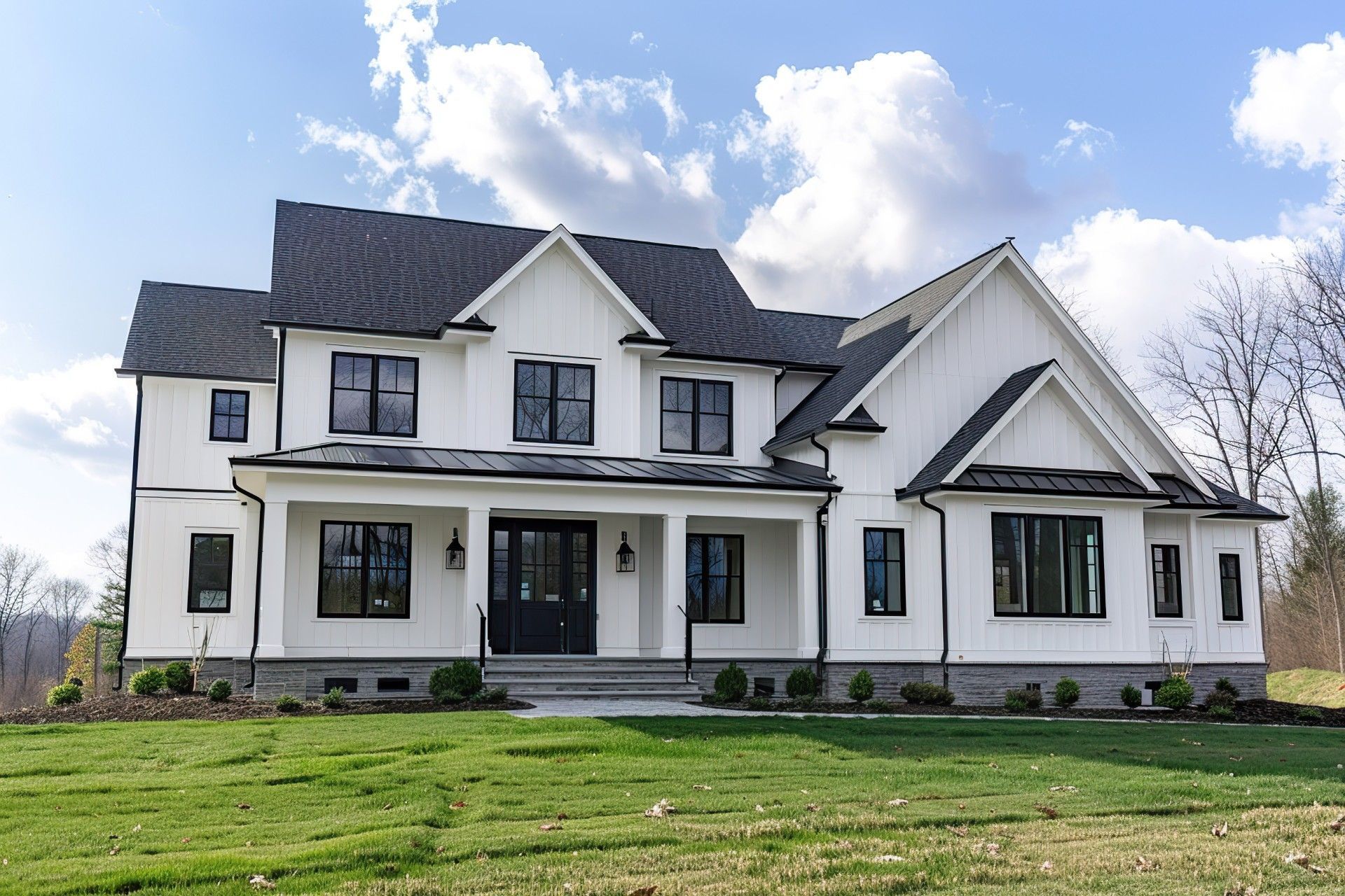 White farmhouse with black accents, on a green lawn under a cloudy sky.