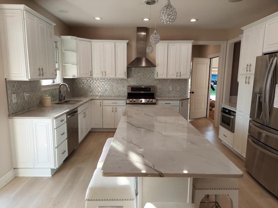 large kitchen island added to a kitchen with white cabinets installed. New marble countertops and stainless steel appliances