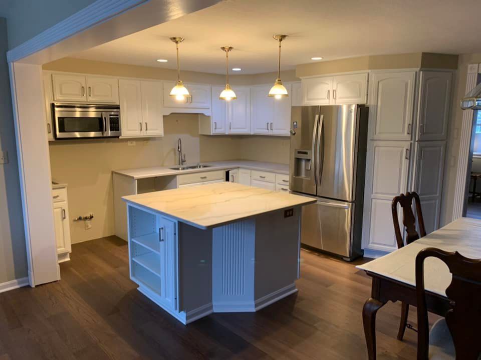 Square kitchen island with white cabinets with new stainless steel cabinets and lighting installed in Pittsburhg