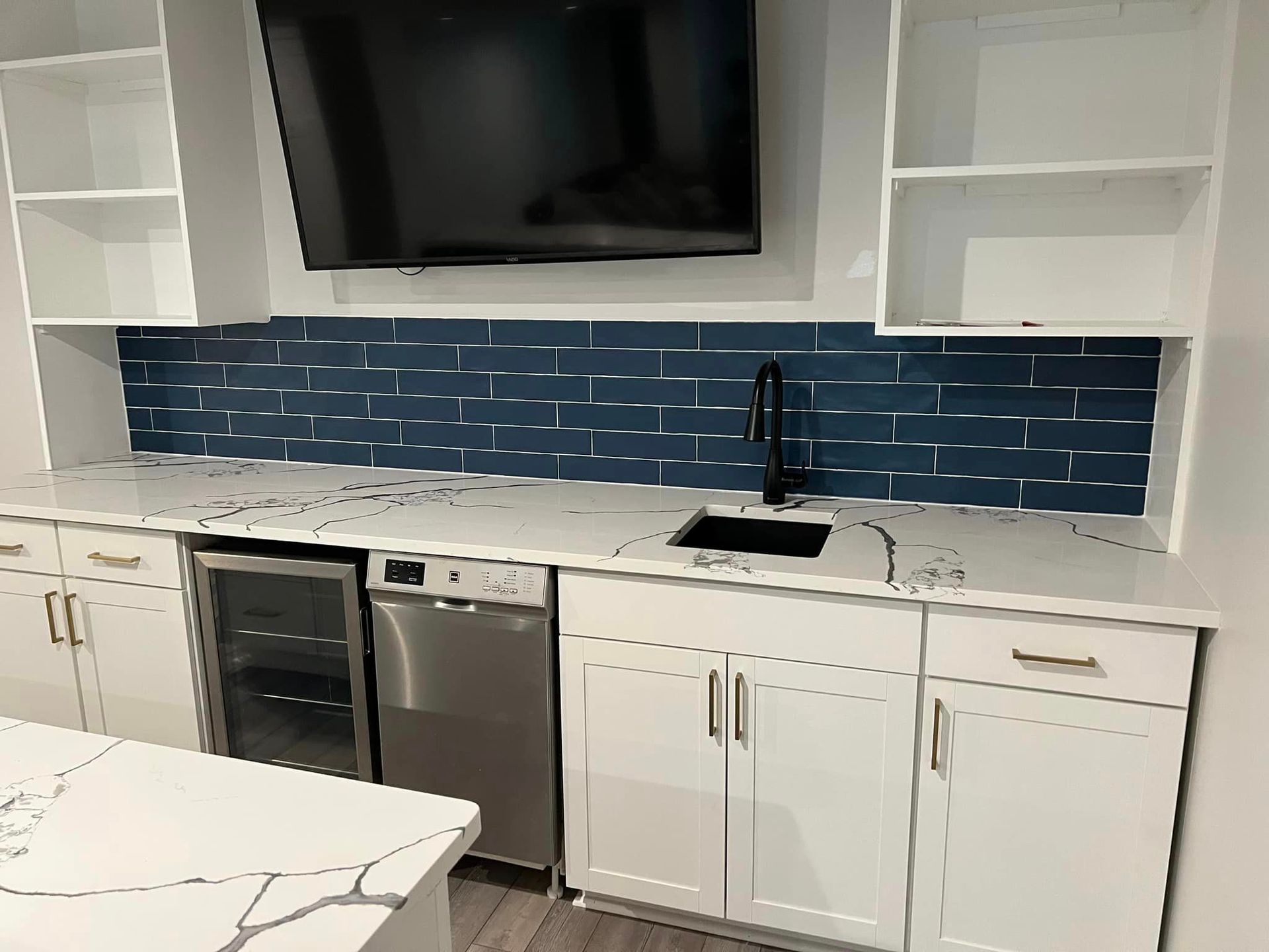 new white kitchen cabinets with blue backsplash, stainless steel appliances and a television
