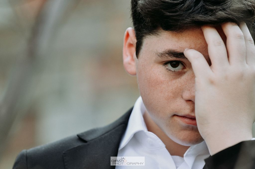 A young man in a suit and white shirt is covering his face with his hand.