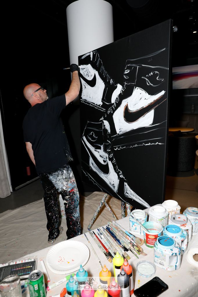 A man is painting a picture of a nike shoe on a canvas.
