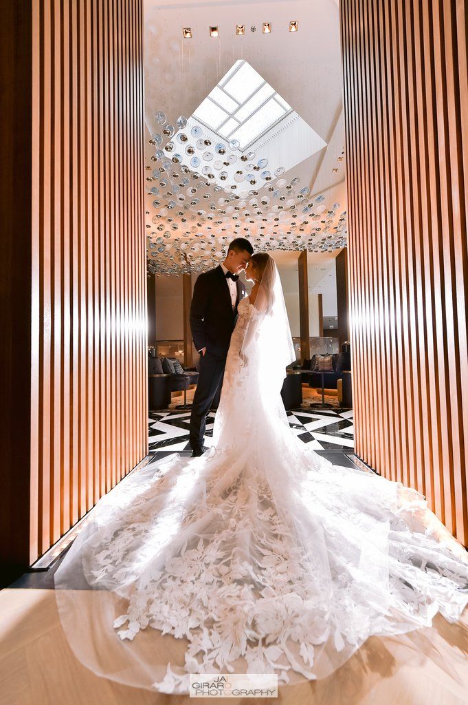 A bride and groom are posing for a picture in a hallway . the bride is wearing a long wedding dress.
