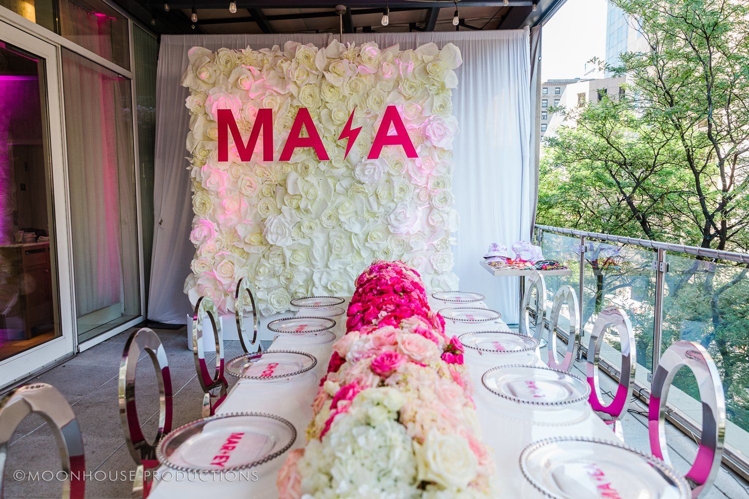 A long table with plates and flowers in front of a wall with flowers.