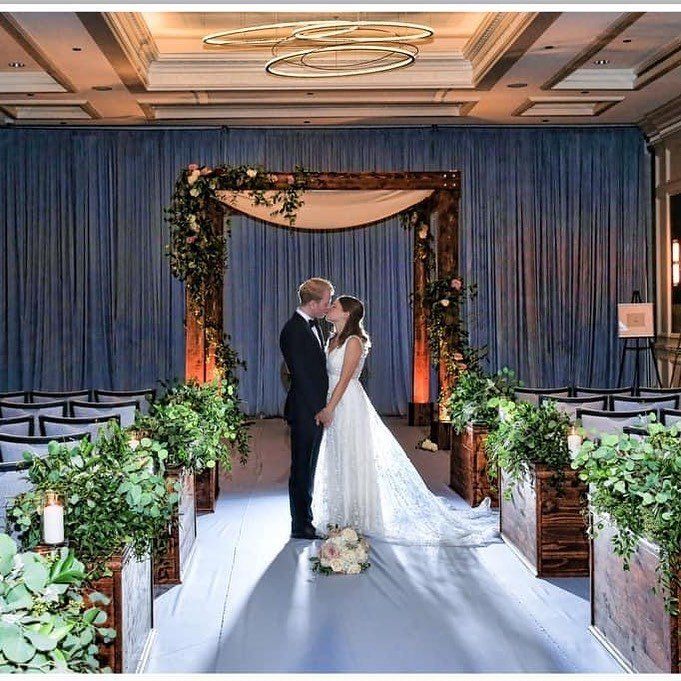 A bride and groom are kissing under a wooden arch at their wedding ceremony.