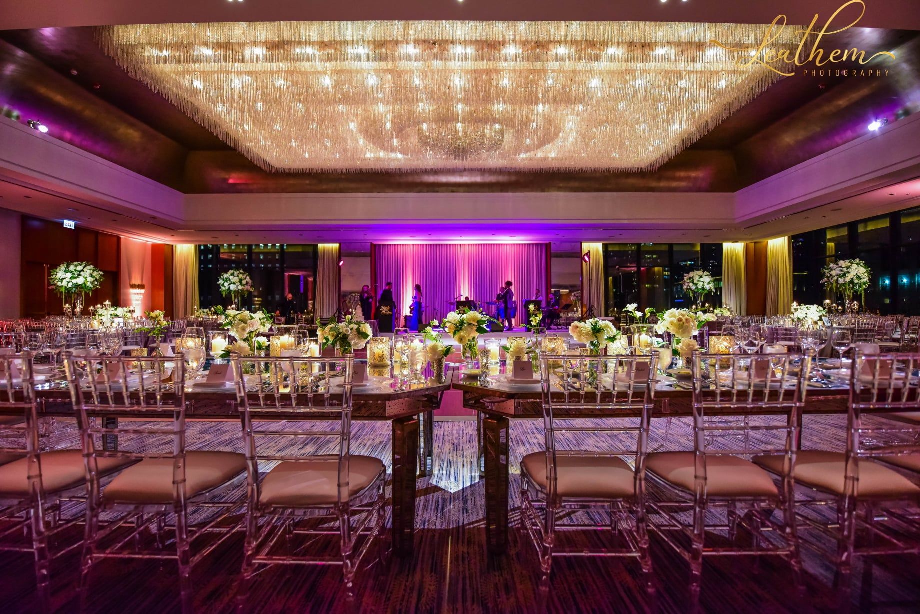 A long table and chairs in a large room with a chandelier.