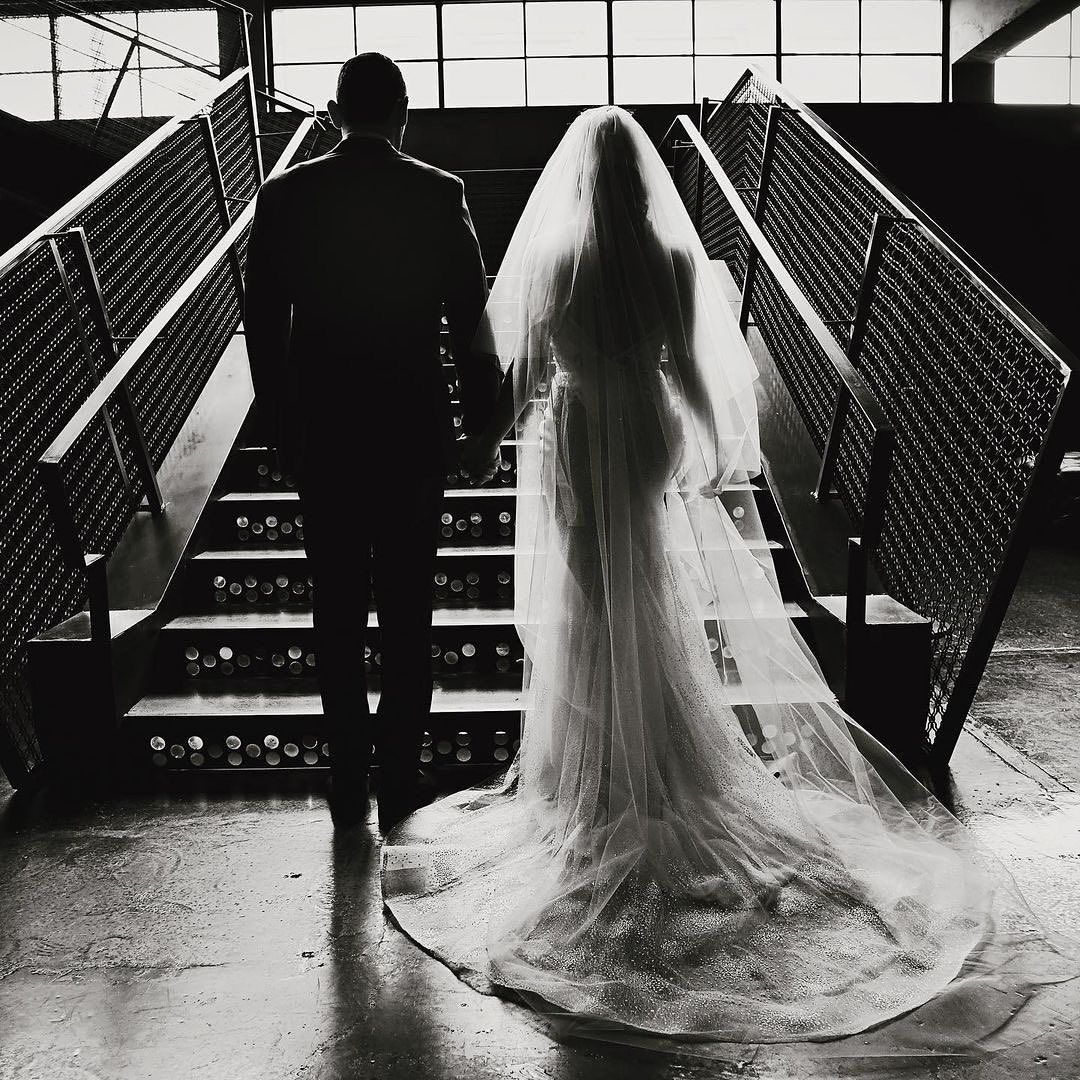 A black and white photo of a bride and groom walking down stairs