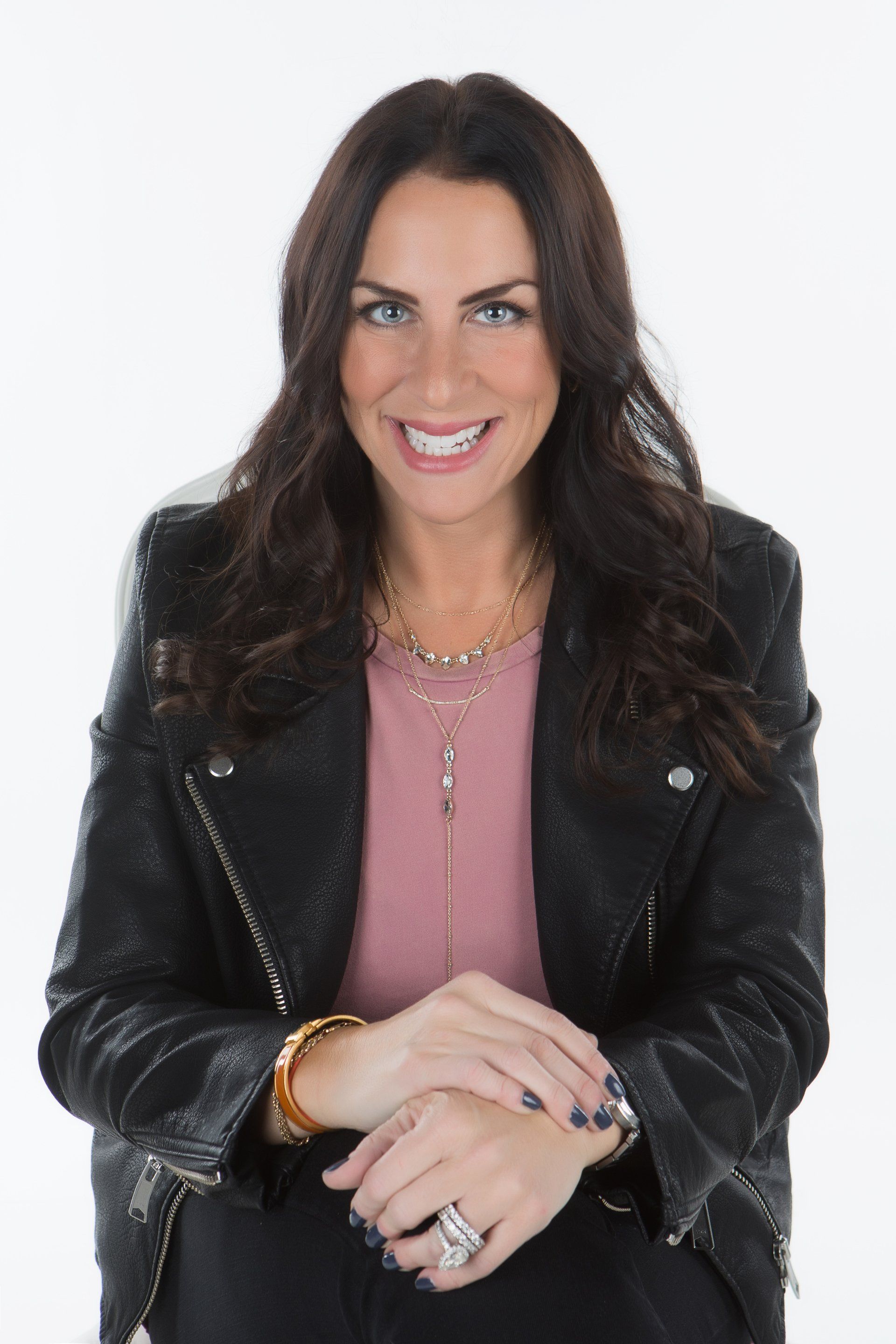 A woman wearing a black leather jacket and a pink shirt is smiling.
