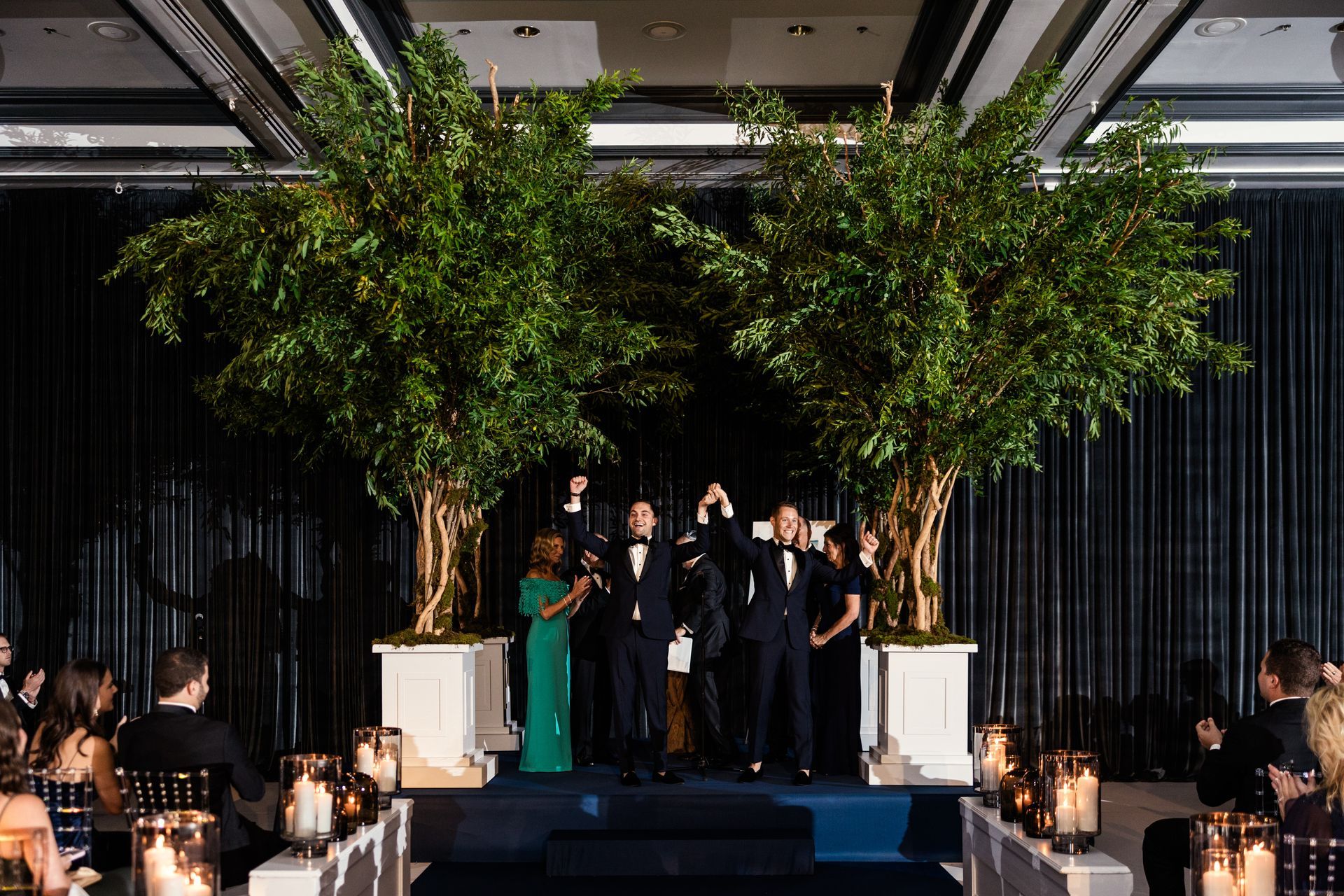 A group of people standing on a stage in front of trees.