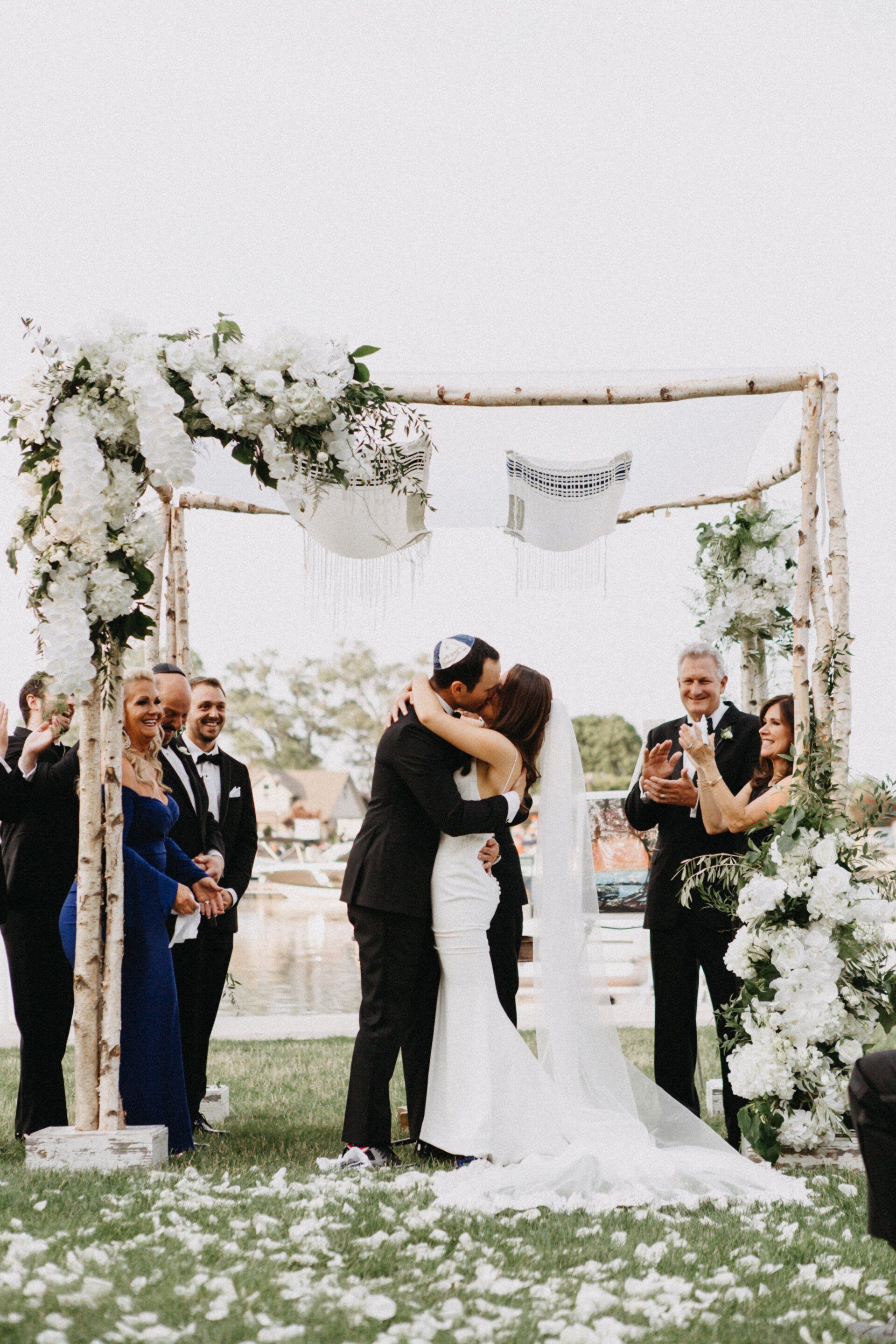A bride and groom kissing at their wedding ceremony under a wooden arch.