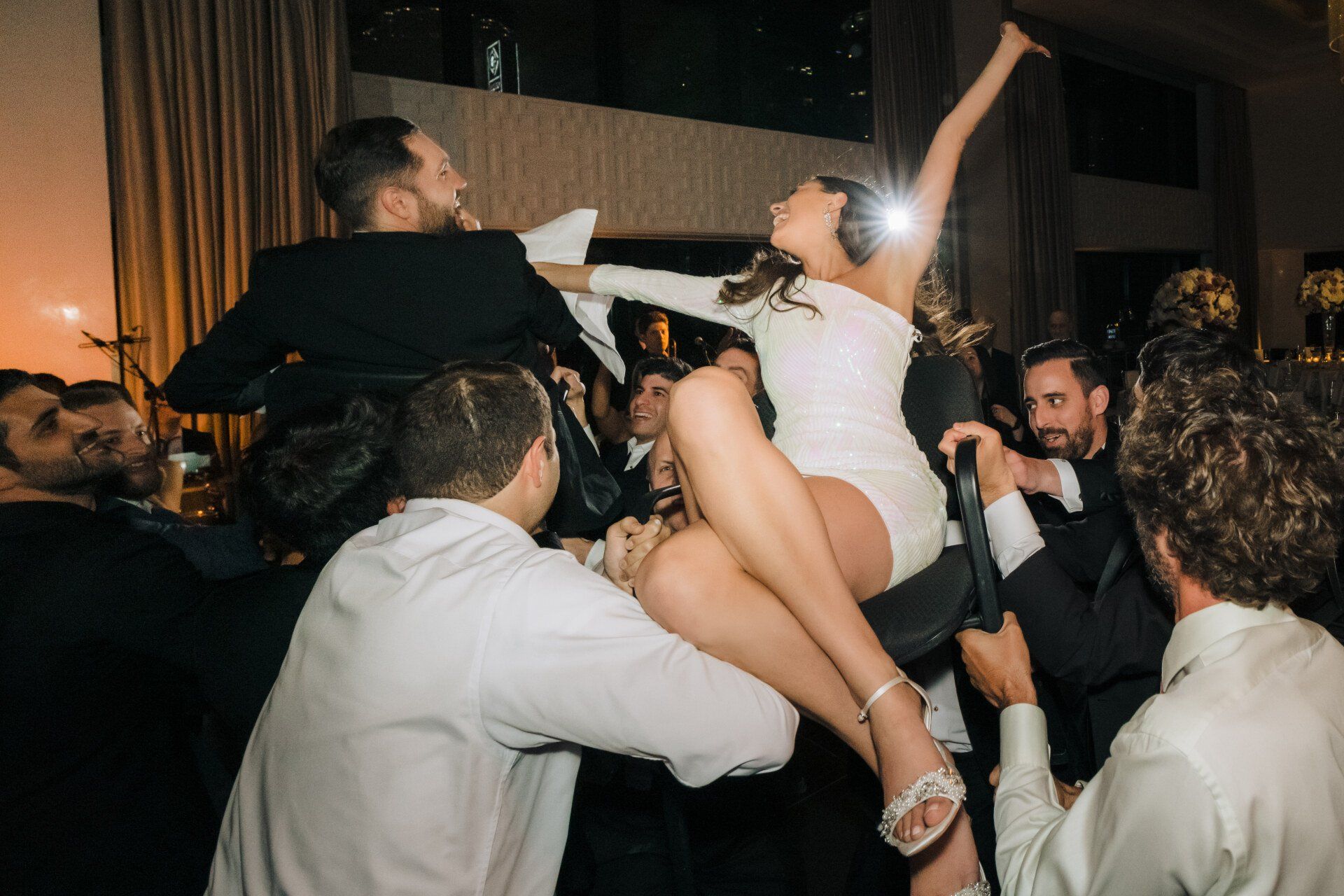 A bride and groom are being carried in the air by their wedding guests.