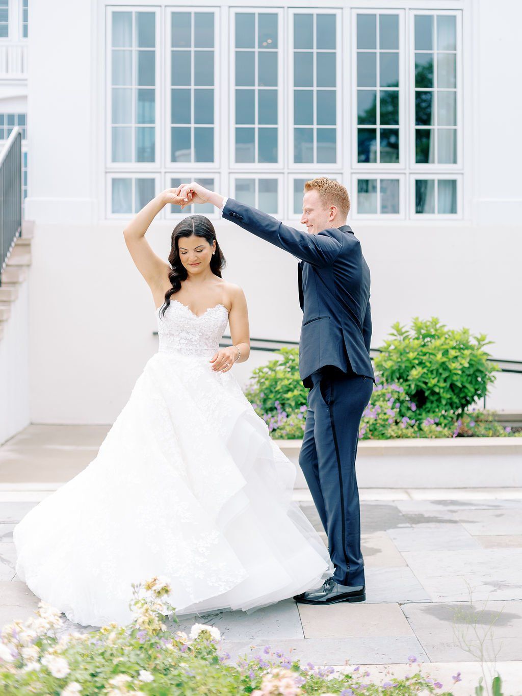 A bride and groom are dancing in front of a white building.