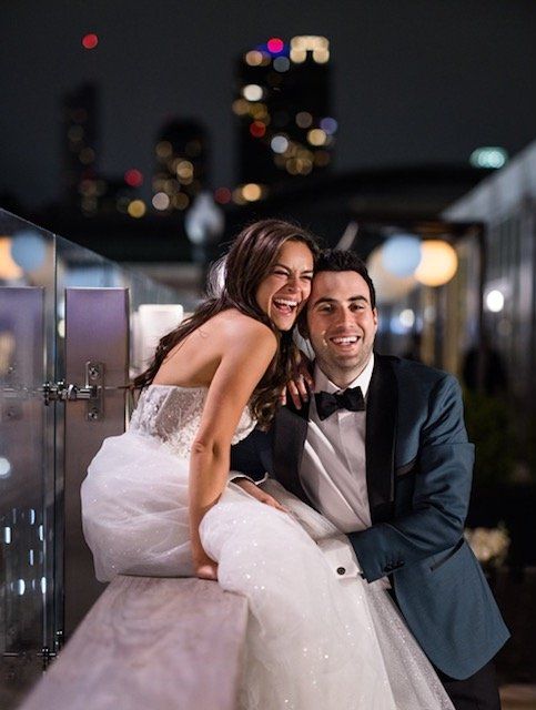 A bride and groom are posing for a picture on a balcony at night.