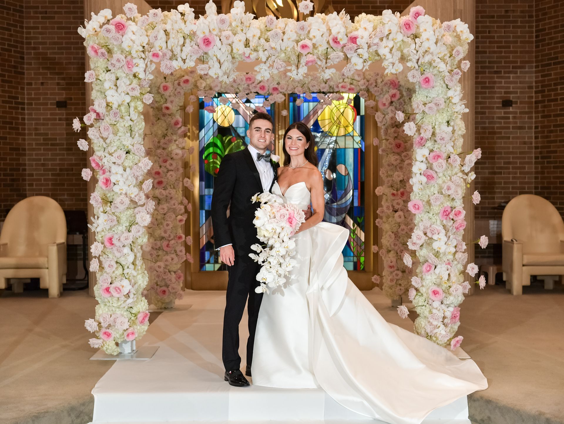 A bride and groom are posing for a picture in front of a stained glass window.