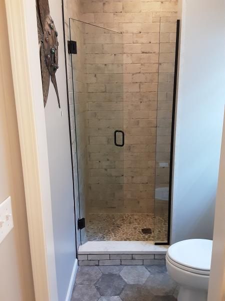 A small bathroom featuring a glass-enclosed shower with beige tiled walls, a pebbled floor, and gray hexagonal floor tiles.