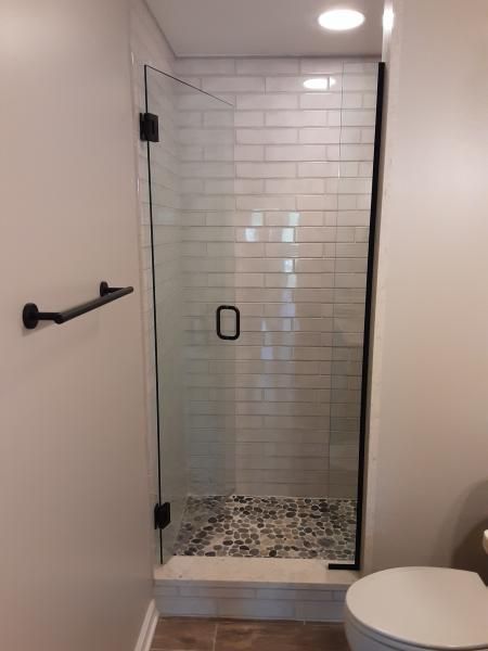 A modern walk-in shower with a glass door, black hardware, white subway tile walls, and a stone pebble floor.