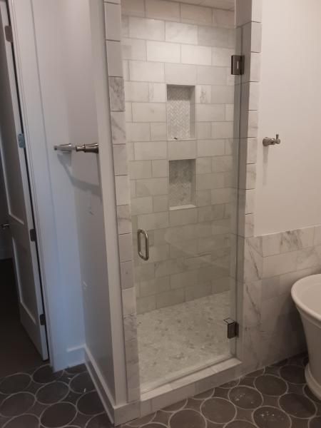 A glass-doored shower enclosure featuring white subway tile, two built-in storage niches, and gray circular floor tiles.