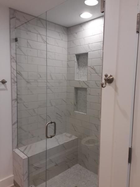 A walk-in shower with white marble-patterned subway tiles, glass door, built-in bench, and two recessed wall niches.