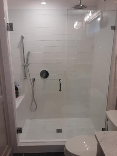 A walk-in shower with white tiled walls, a glass door, handheld shower head, and a built-in bench seat.