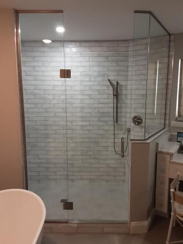 A glass-enclosed walk-in shower with white brick-style tiles, a handheld showerhead, and a corner glass return panel.