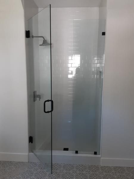 A glass walk-in shower door with matte black hardware installed in a white tiled bathroom.