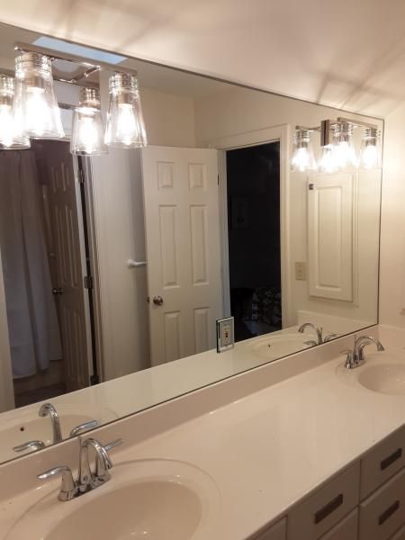 Bathroom vanity with white countertop, double sinks, chrome faucets, and a large wall mirror with four-light fixtures.