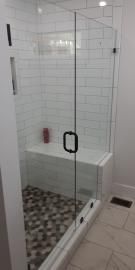 A walk-in shower with a glass door, white subway tile walls, a built-in bench, and a textured pebble floor.