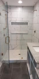 A modern tiled walk-in shower with a glass door, a built-in recessed shelf, and dark floor tiles.