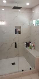 Modern walk-in shower with white marble-patterned tiles, a square black rainfall showerhead, and a built-in tiled bench.