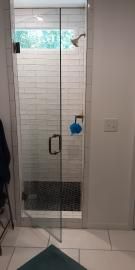 A glass-door shower with white subway-tiled walls, a dark stone floor, a rainfall showerhead, and a blue bath sponge.