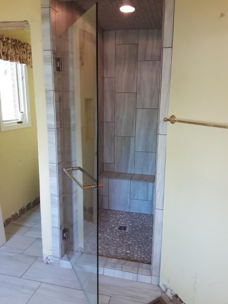 A glass-enclosed shower with tiled walls, a built-in bench, and a pebble floor, located in a yellow-walled bathroom.