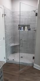 A glass-enclosed shower with gray tiled walls, a built-in corner seat, and a recessed shampoo niche.
